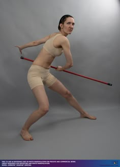 a woman holding a stick in her right hand and posing for the camera on a gray background