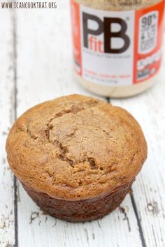 a close up of a muffin on a wooden surface with a jar of peanut butter in the background