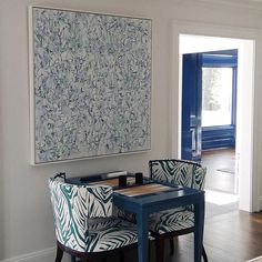 two chairs and a table in front of a large painting on the wall above them