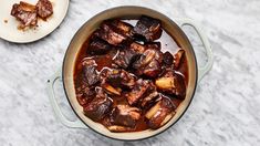 a pot filled with meat and sauce next to a spoon on a marble counter top