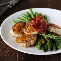 scallops, asparagus and bacon on a white plate next to silverware