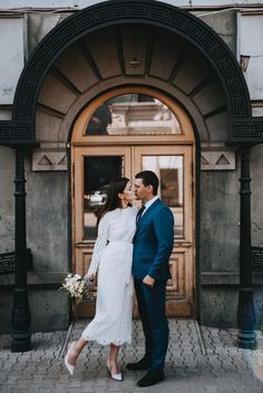 a man and woman are standing in front of a building with an arched doorway holding hands