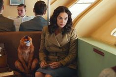 a woman sitting on a train next to a monkey and other people in the background