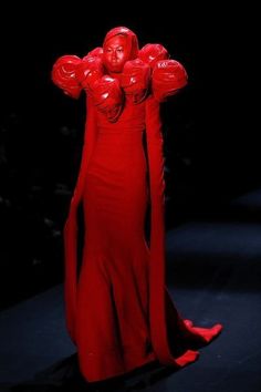 a woman in a red dress with her arms up and hands behind her head, standing on a runway