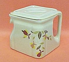 a white ceramic teapot with yellow and red leaves on it's lid, sitting on a pink surface