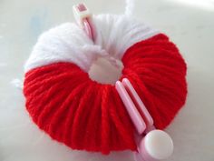 a red and white ball of yarn next to a pink toothbrush on a white surface