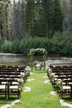 an outdoor ceremony set up with chairs and flowers on the grass next to a river