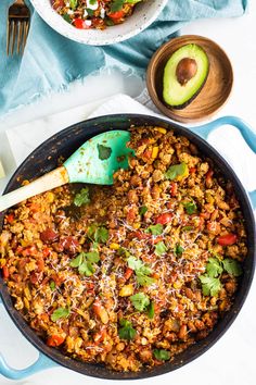 a skillet filled with rice and vegetables next to an avocado on the side