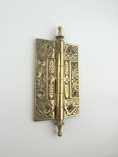 an antique brass door hinge with decorative designs on the front and back sides, mounted on a white wall