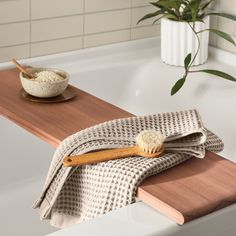 a wooden brush sitting on top of a bath tub next to a bowl and towel