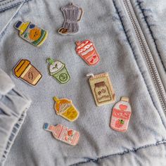 several small pins are placed in the back pocket of a jean jacket, which is decorated with food and drinks