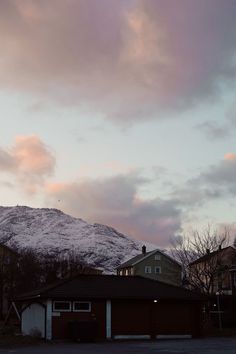 the sky is pink and purple as the sun goes down over some houses in front of a snow covered mountain