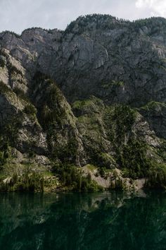 the mountains are reflected in the water near some trees and bushes on the side of the mountain