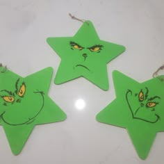 three green star shaped ornaments with yellow eyes and nose drawn on them, sitting on a white surface