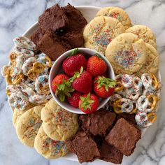 a white plate topped with lots of cookies and strawberries next to chocolate brownies