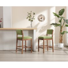 two green chairs in front of a counter with plants on the side and a clock mounted to the wall