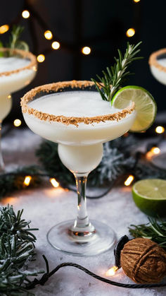 two margaritas with lime and rosemary garnish on the rim, surrounded by christmas lights