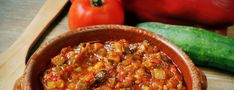 a wooden bowl filled with food on top of a table next to tomatoes and cucumbers