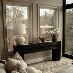 a living room with two large windows and a table in front of the window that has candles on it