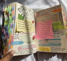 an open book with colorful sticky notes and writing on the pages is held in someone's hand