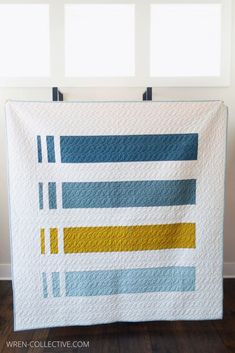 a blue and yellow striped quilt hanging on a wall in front of a white window