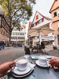 two people sitting at an outdoor table with cups and saucers in front of them