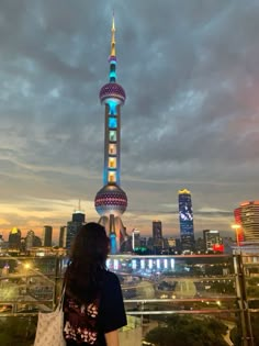 a woman standing on top of a tall building next to a cityscape at night