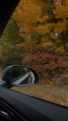 a car's rear view mirror is shown in front of trees with yellow and red leaves