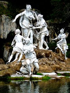 the statue is surrounded by other statues in front of some rocks and water, with trees in the background