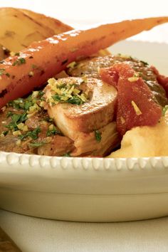 a white bowl filled with meat and vegetables on top of a table next to bread