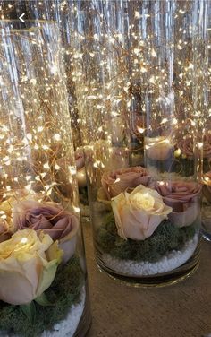 some glass vases with flowers and lights in them