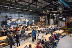 a large group of people standing around tables in a room filled with wooden benches and beer kegs