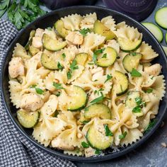 pasta with zucchini, chicken and parsley in a black bowl next to sliced cucumbers