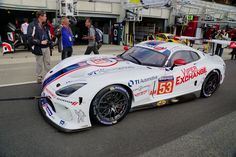 a white race car parked on the side of a road with people standing around it