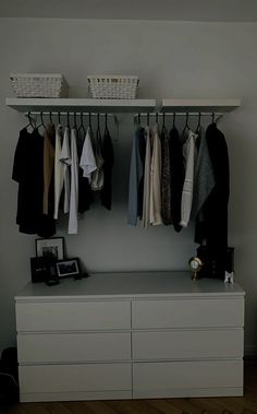 an organized closet with clothes hanging on the rails and baskets above it, next to a white dresser