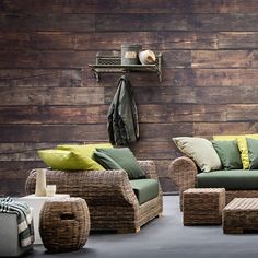 two wicker couches and one chair with green cushions in front of a wooden wall