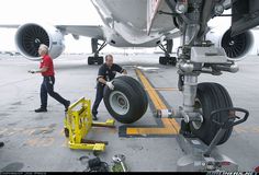 two men standing next to each other near an airplane on the tarmac with wheels attached