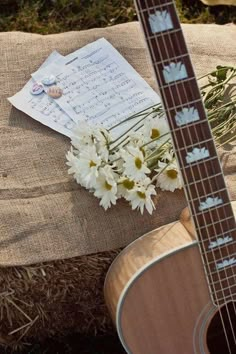 a guitar and some flowers sitting on top of a pillow next to a sheet of paper