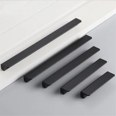 four black handles are shown on the side of a white door and one is in front of it