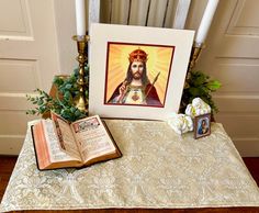 an open book sitting on top of a table next to a painting and candle holders