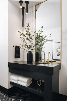 a black and white bathroom with gold accents, plants and towels on the sink counter