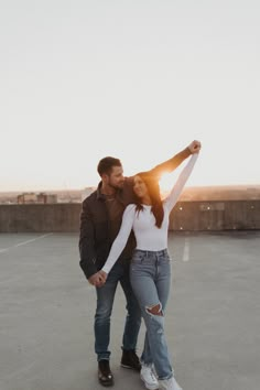 a man and woman standing in an empty parking lot holding each other's arms