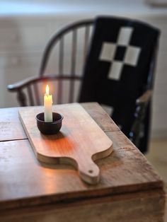 a lit candle sits in a bowl on top of a cutting board next to a chair