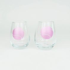 two wine glasses sitting side by side on a white surface, one has a pink ball in the middle