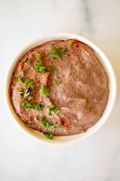 a white bowl filled with hummus and garnished with parsley on top