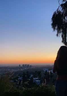 a woman standing on top of a lush green hillside next to a tall building at sunset