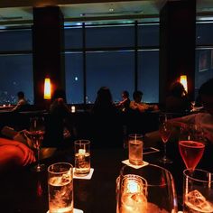 people sitting at a table with wine glasses and drinks in front of large windows overlooking the city