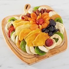 a wooden platter filled with sliced fruit and veggies on top of a marble counter