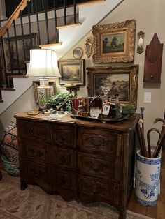 a wooden dresser sitting under a stair case next to a lamp and pictures on the wall