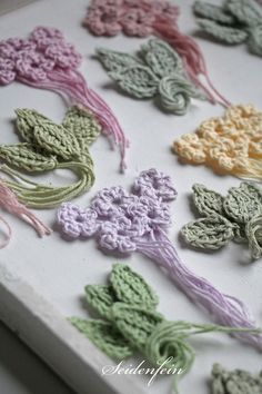 many crocheted flowers are arranged on a white board with pink, green, yellow and purple yarn